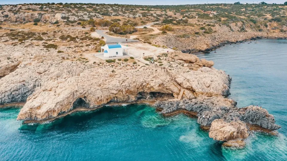 Aerial view of Ayii Anargyroi wedding chapel on the rocky coastline of Ayia Napa, Cyprus, overlooking turquoise Mediterranean sea