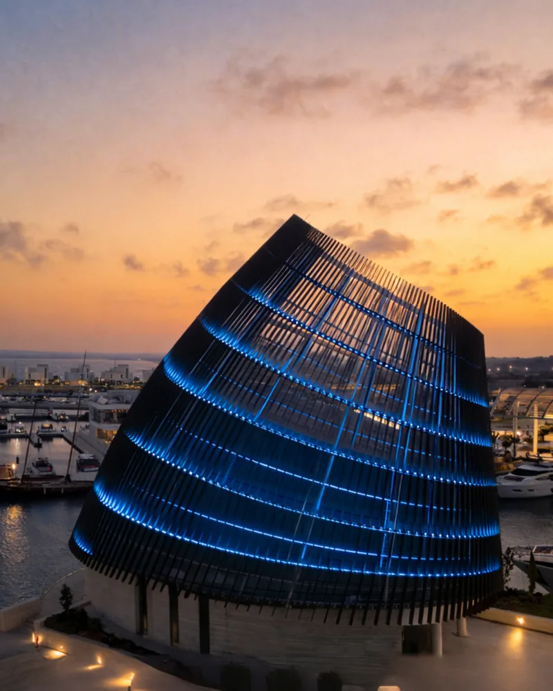 Modern architectural wedding venue at Ayia Napa Marina illuminated at sunset, overlooking luxury yachts and the Mediterranean Sea in Cyprus.