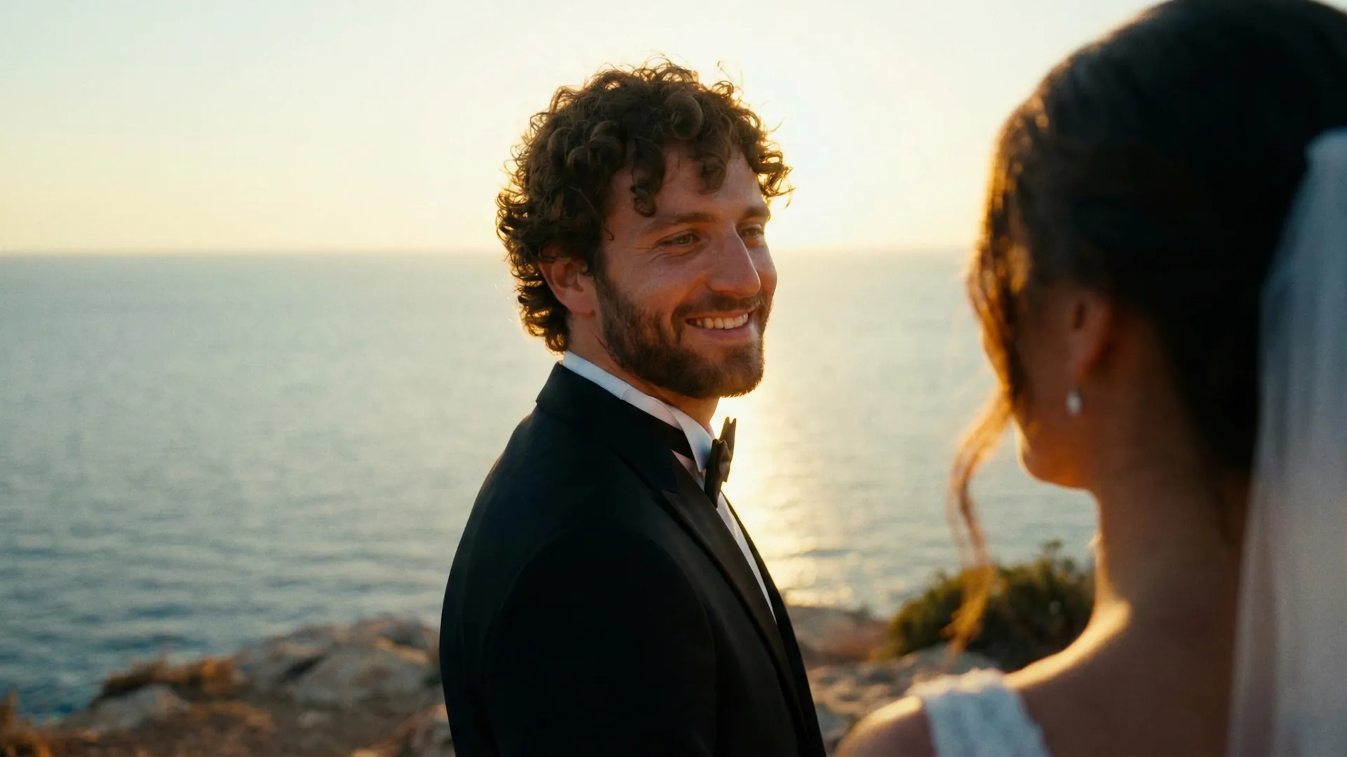 Groom smiling at his bride during a seaside wedding portrait at sunset, captured in a romantic Mediterranean landscape