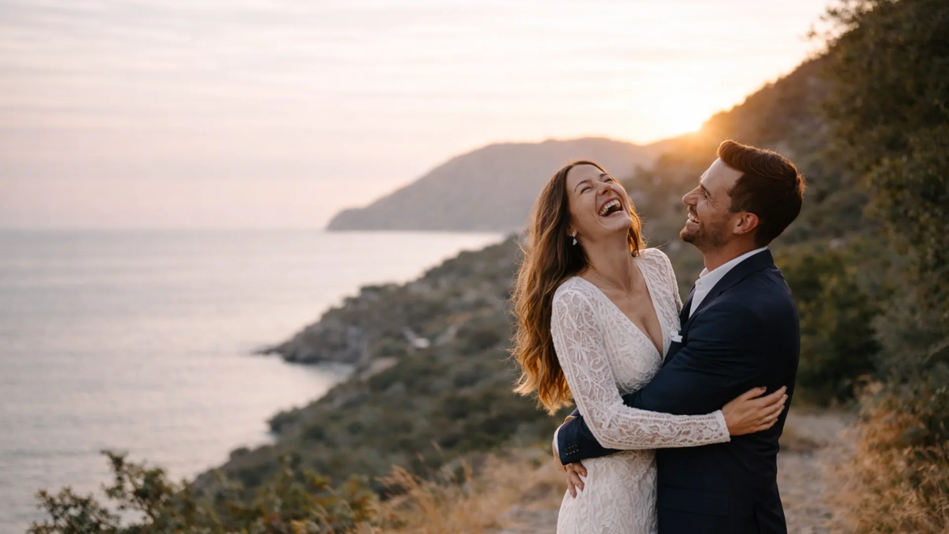 Bride and groom embracing joyfully on a Mediterranean cliffside at sunset, captured during golden hour on their wedding day.