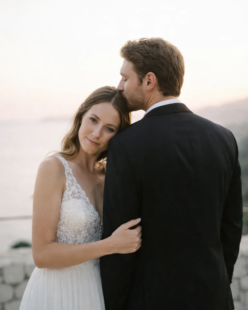 Bride resting her head on the groom’s shoulder as he kisses her temple during a coastal sunset wedding portrait.